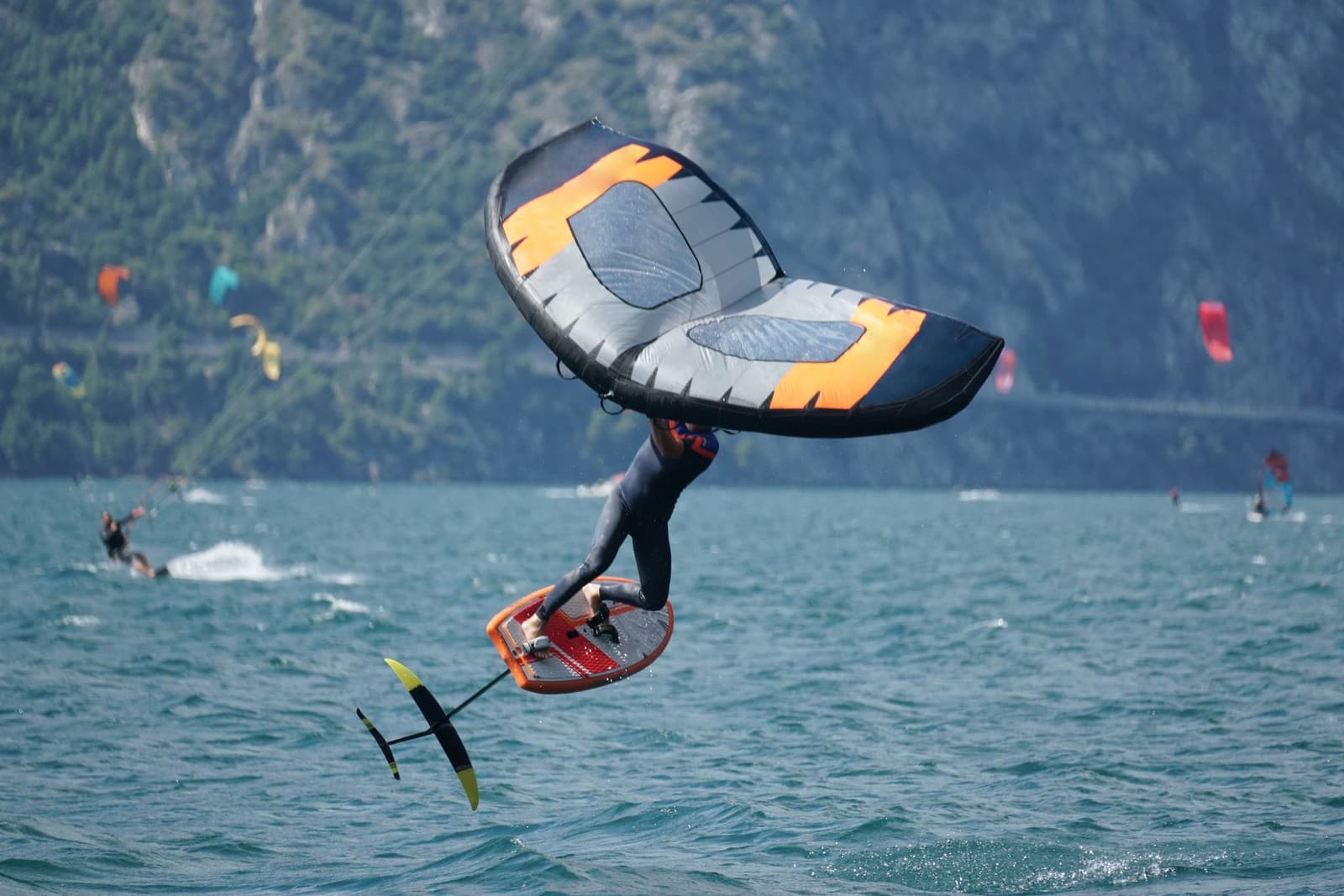 A thrill-seeker catches air while wing foiling on Lake Garda near Riva del Garda, surrounded by fellow wind and kite surfers in one of Italy’s top spots for water sports and adventure.