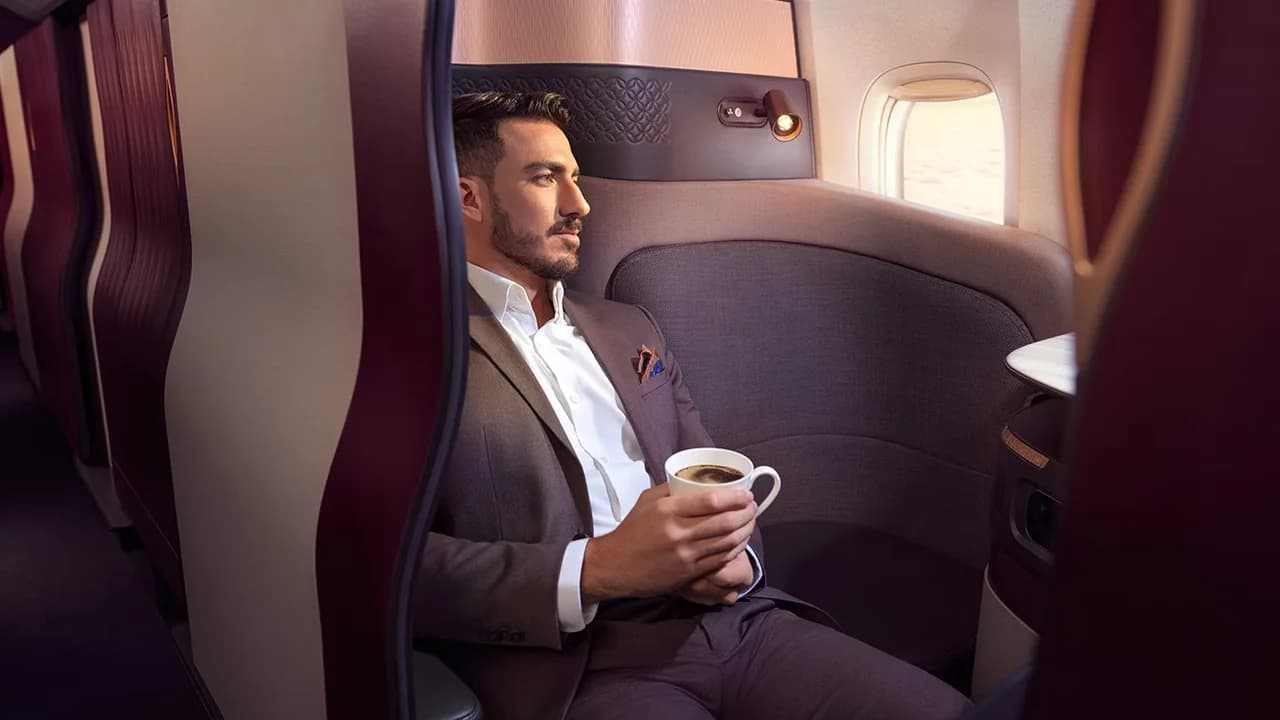 Qatar Airways QSuite with burgundy quilted door panels and teal LED accents — the best business class product in the sky at wholesale pricing
