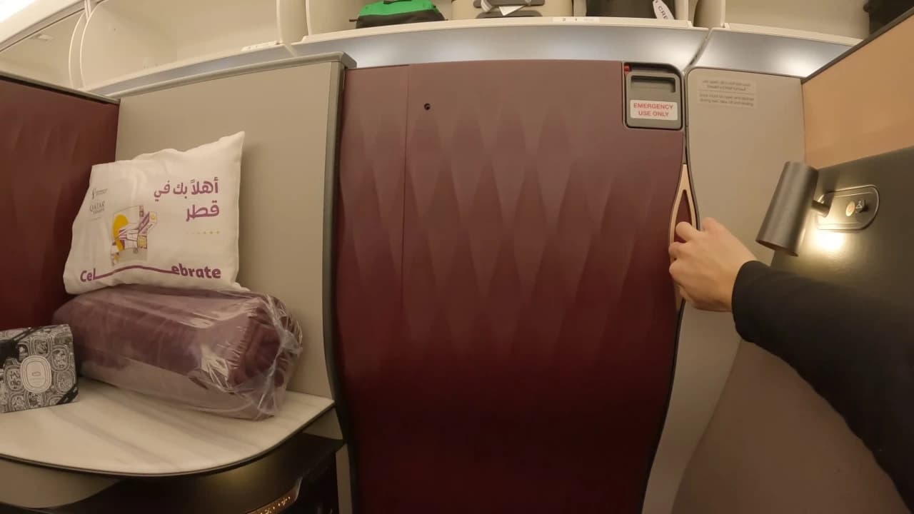 Qatar Airways QSuite cabin with sliding privacy doors closed on the Boeing 777-300ER — the signature burgundy and grey palette creates an upscale atmosphere