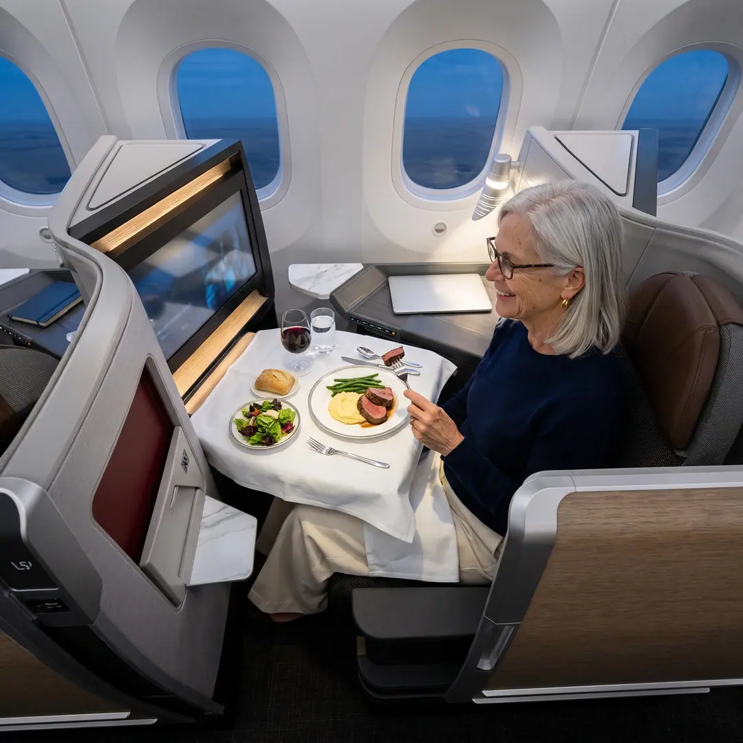 Seen from above: Linda at dinner in her Business Class suite, beef tenderloin, salad and a glass of red wine on a white tablecloth, dusk blue outside the windows