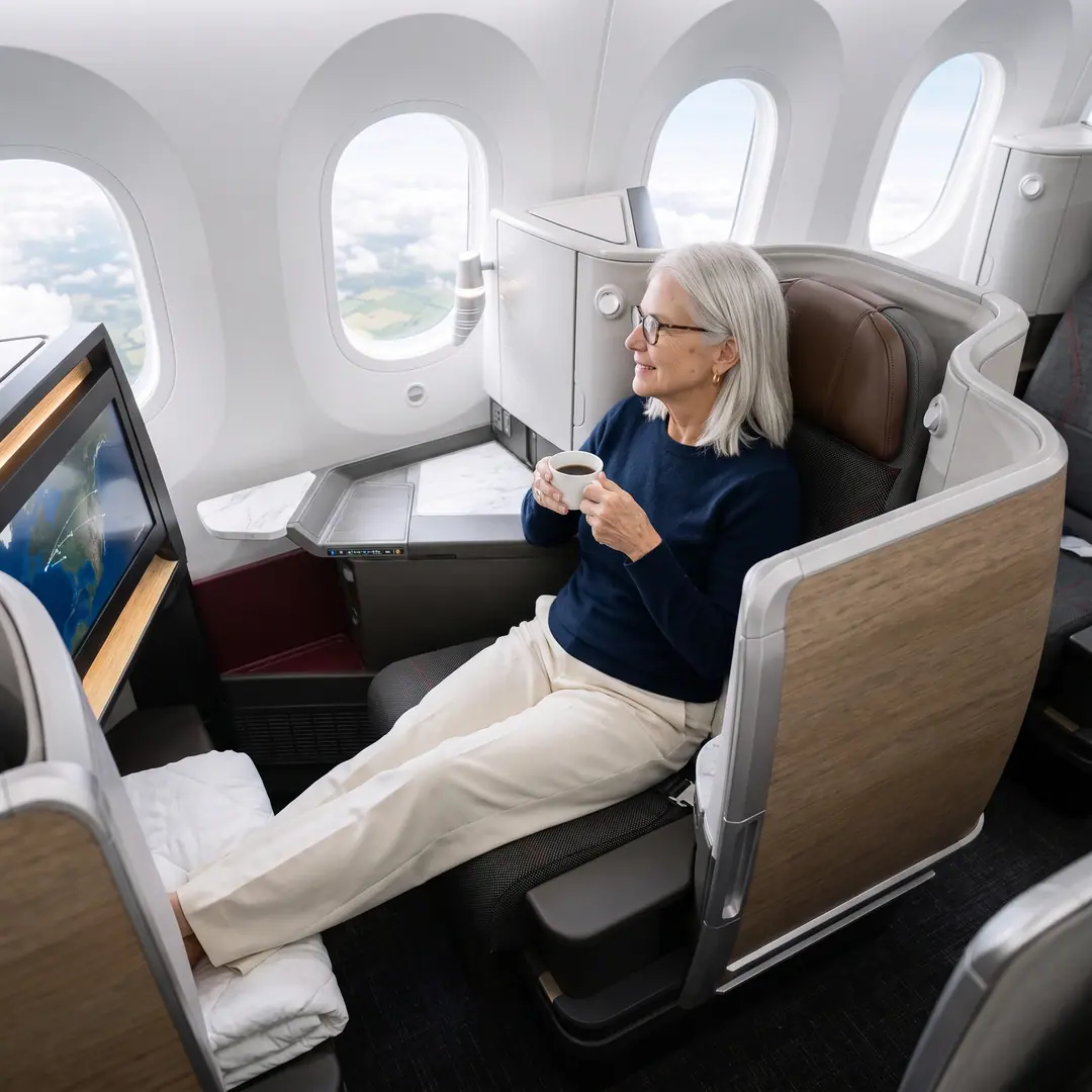 Seen from above: Linda, rested, holding a coffee in her Business Class suite with her legs stretched out, looking out of the window at morning clouds and the fields of France