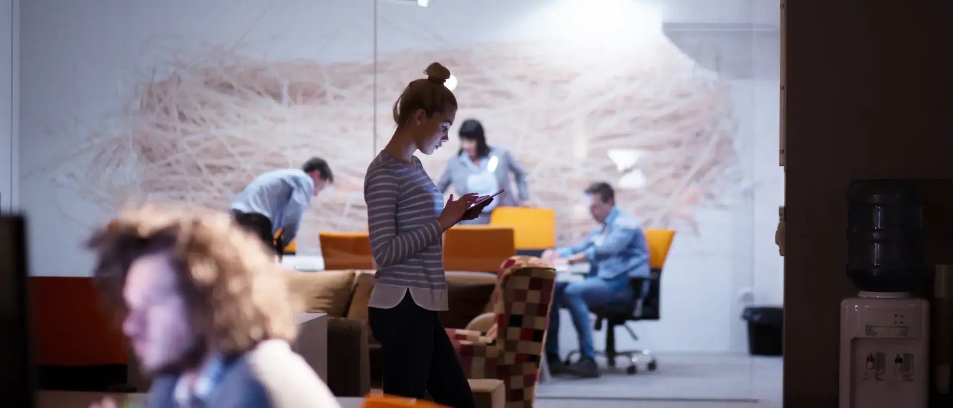 Travel managers at work in the office: one checks a message on her phone while colleagues plan at a table behind the glass